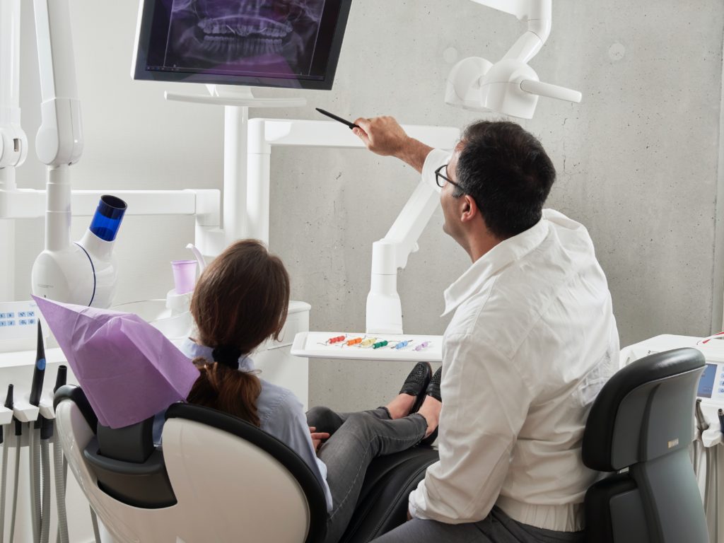 Man and woman sitting in chairs in the dentist office with a teeth diagram