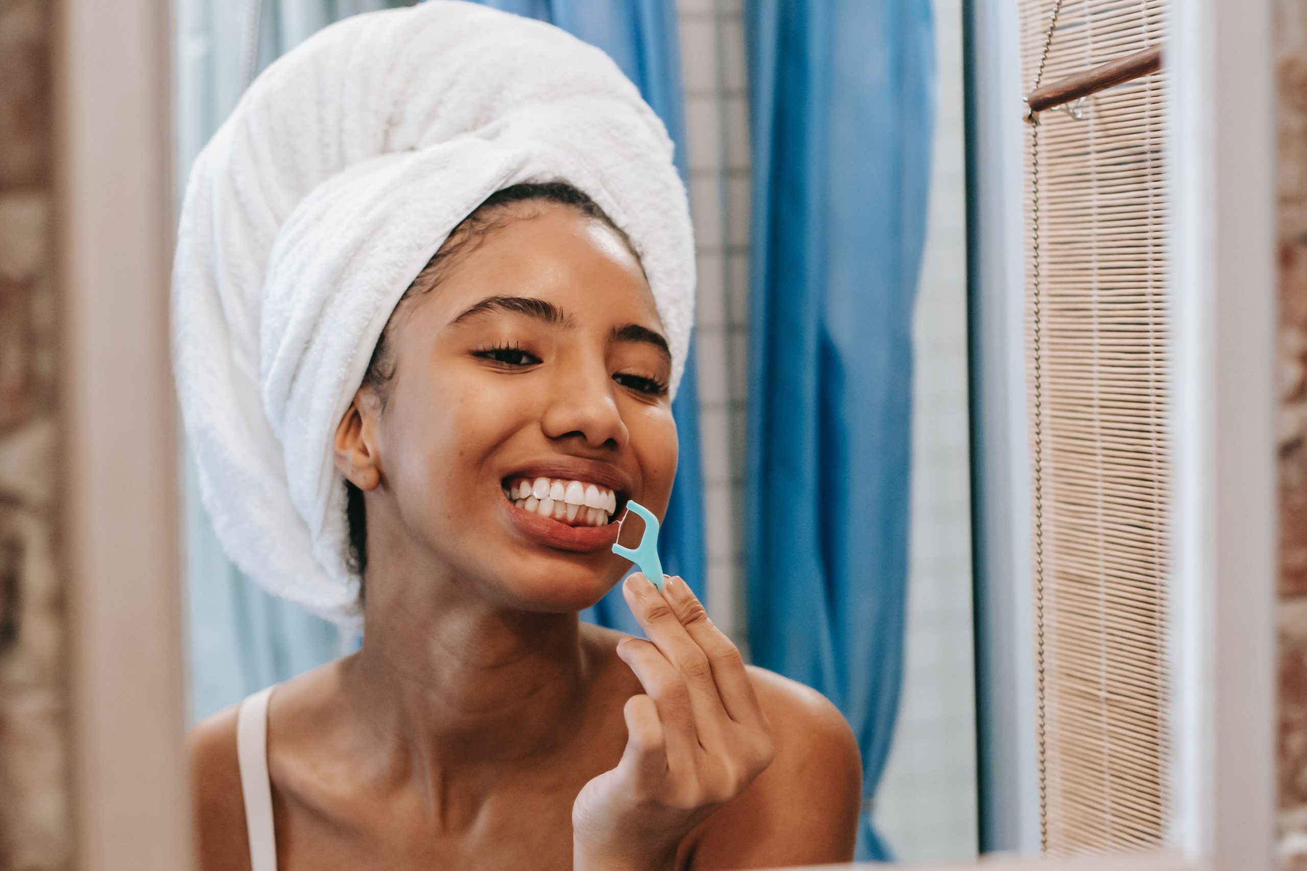 A young woman with a floss pick looks at her teeth and gums.