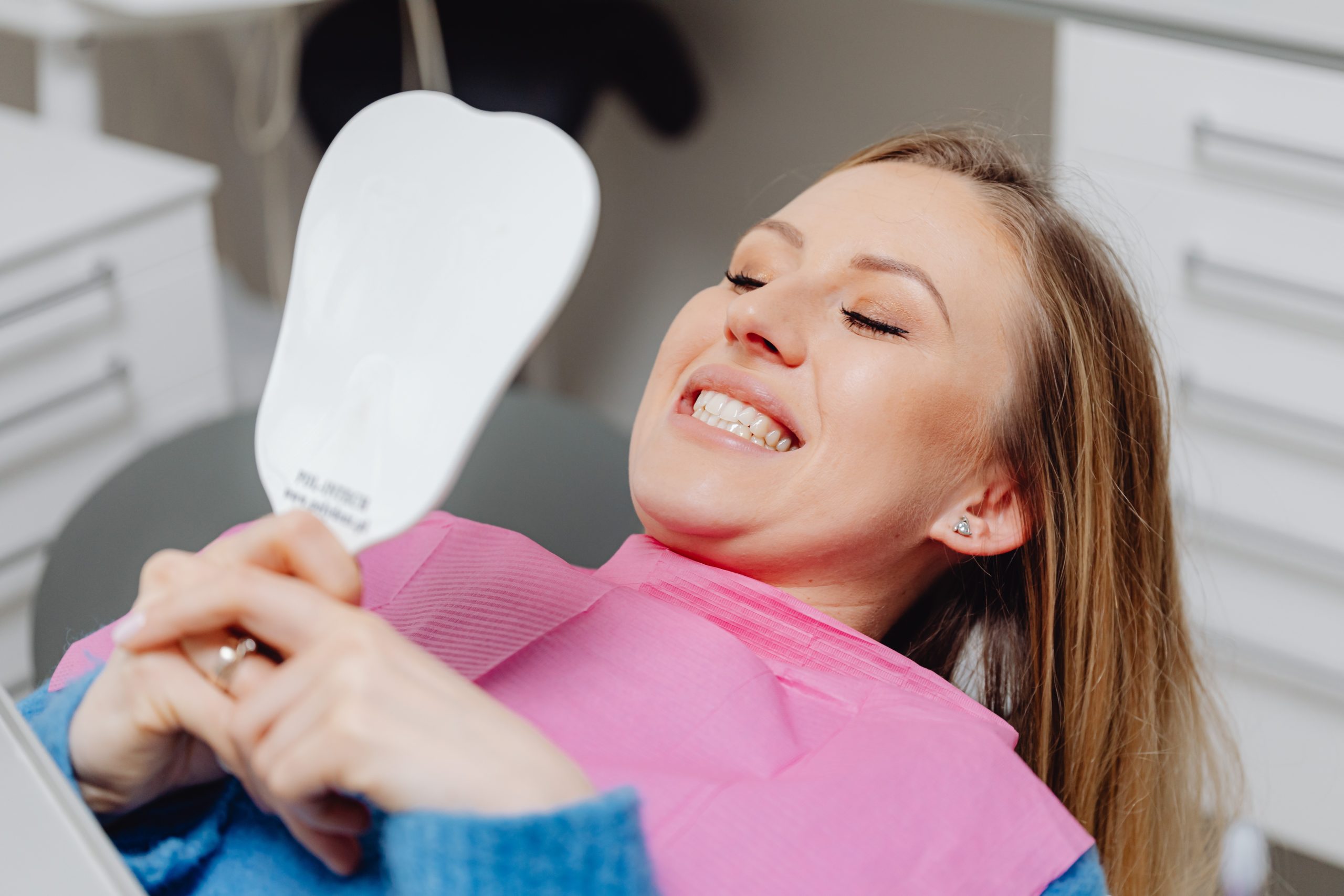 woman looking at teeth in hand mirror at the dentist’s office