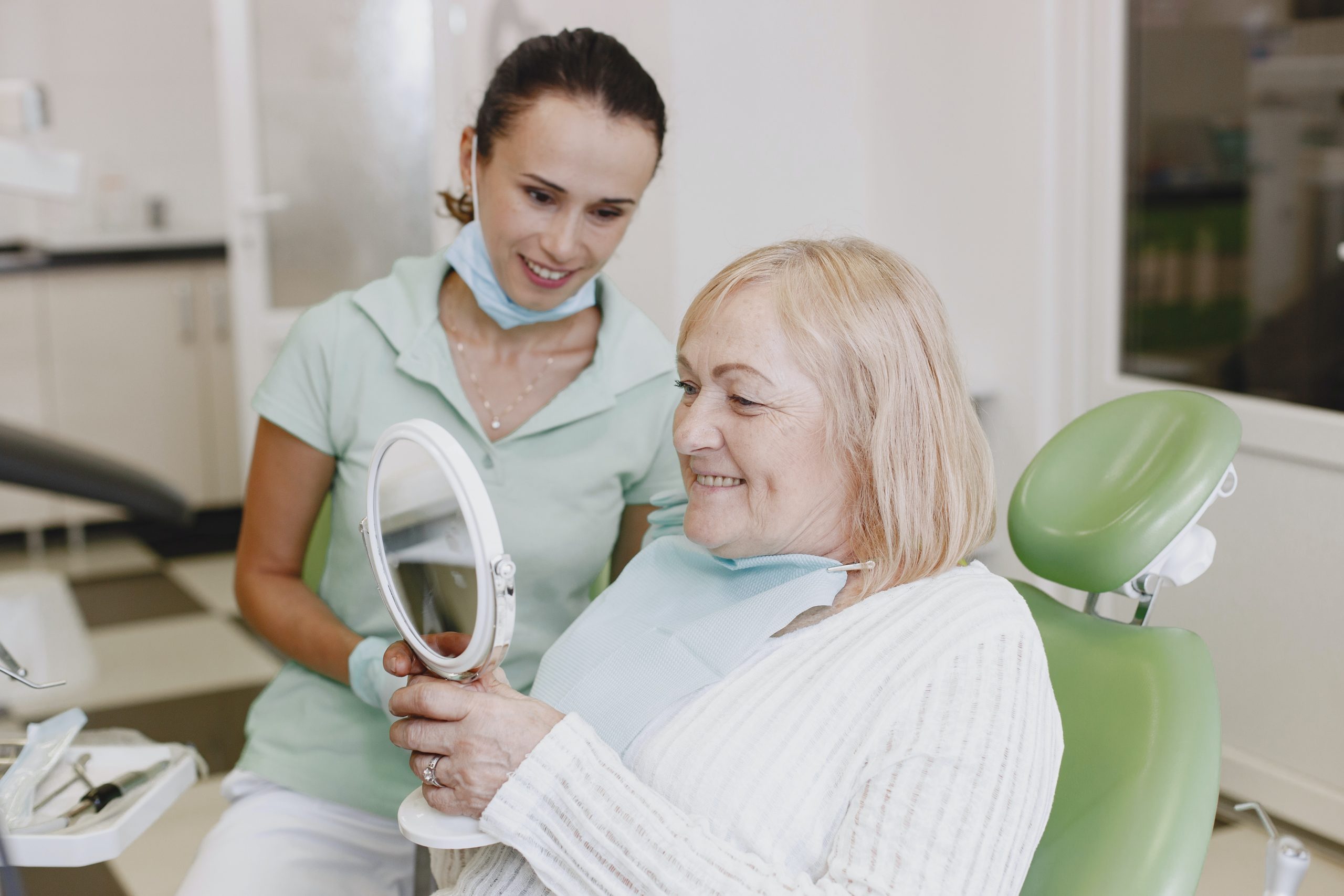 An older woman looks in the mirror at her new dentures.