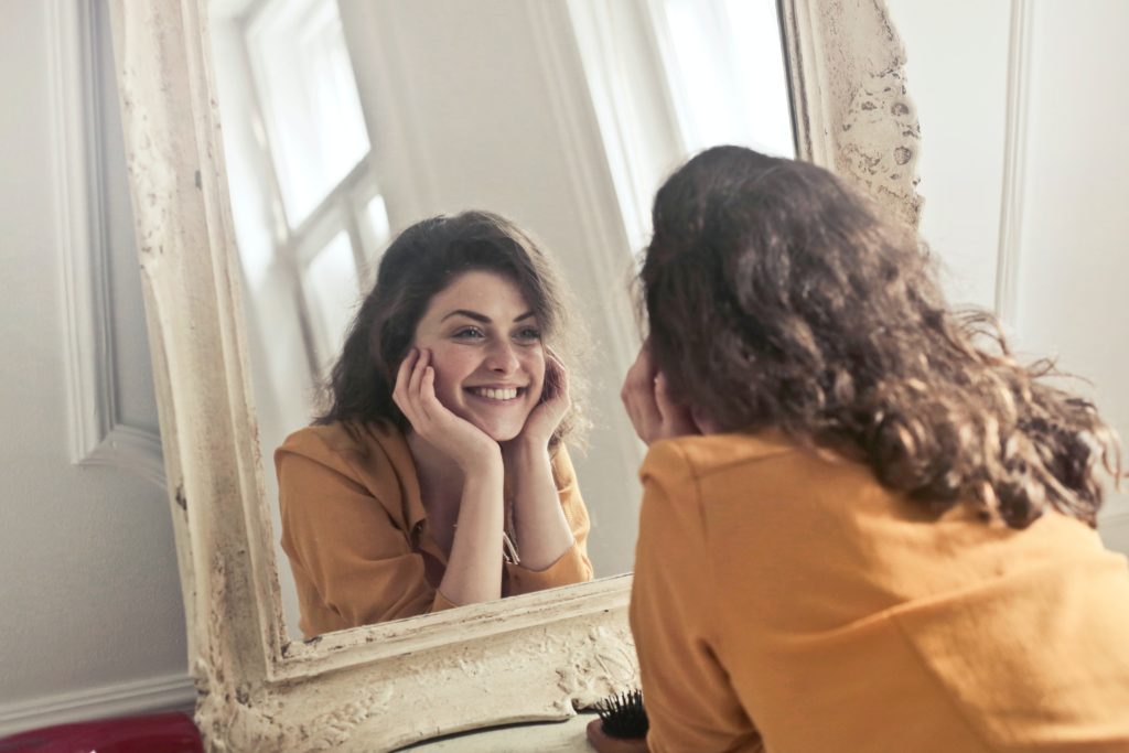 A young woman with natural-looking dentures smiles in a mirror. 